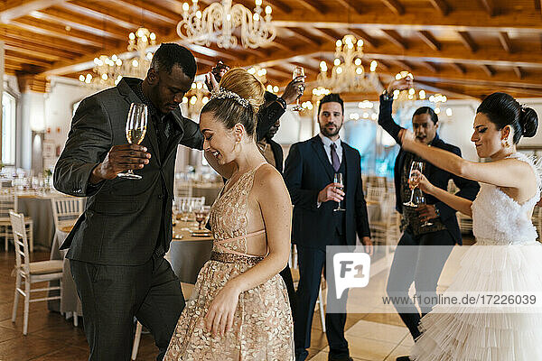 Male and female friends dancing while holding champagne flute at banquet