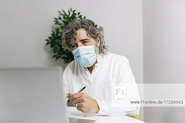 Geschäftsmann mit Gesichtsschutzmaske bei der Arbeit am Laptop im Büro während der COVID-19