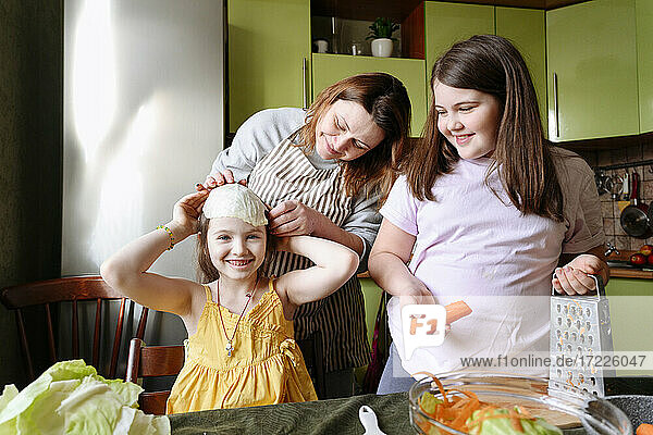Verspielte Mutter und lächelnde Töchter bei der Zubereitung von Speisen in der Küche zu Hause