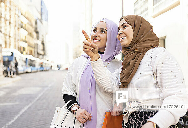 Young woman pointing to female friend while shopping in city