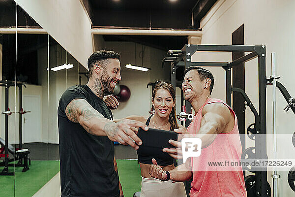 Cheerful friends taking selfie through smart phone at gym