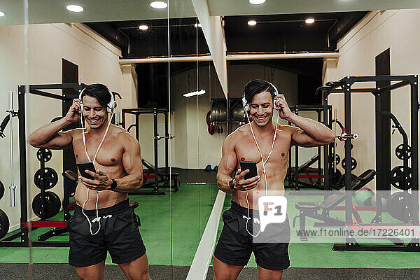 Mid adult athlete using mobile phone while adjusting headphones in gym