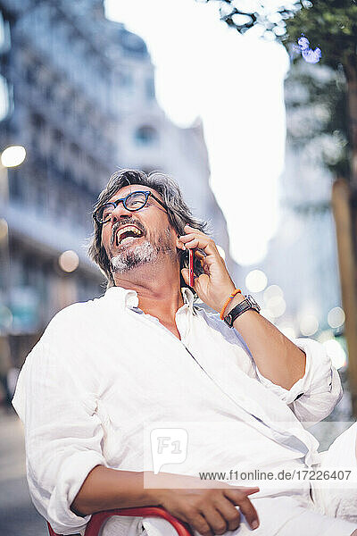 Senior man laughing while talking on mobile phone at sidewalk cafe in Madrid
