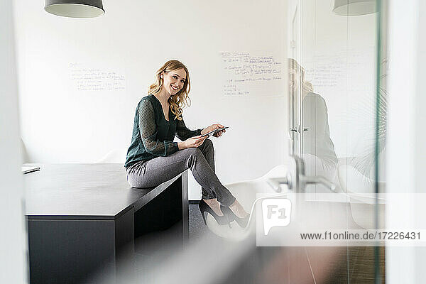 Smiling female entrepreneur sitting with digital tablet on conference table in board room