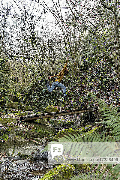 Carefree man jumping over footbridge in forest
