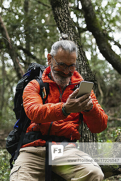 Smiling senior man using mobile phone in forest during weekend