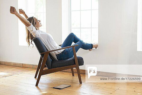 Frau streckt Arme aus  während sie auf einem Stuhl vor einem Fenster sitzt