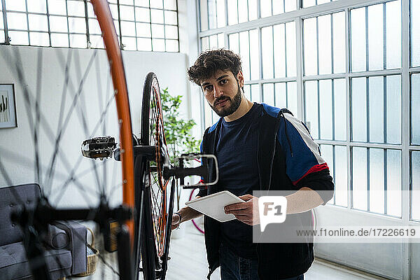 Junger Mann mit digitalem Tablet bei der Reparatur eines Fahrrads zu Hause