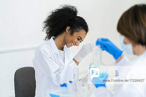 Smiling female researcher working with coworker while experimenting in laboratory