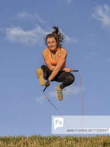 Young woman jumping rope in front of blue sky