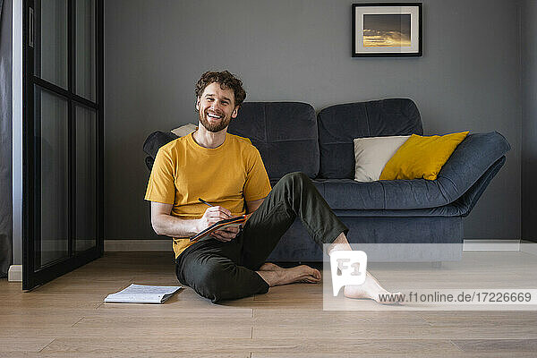 Smiling man sitting with book on floor at home
