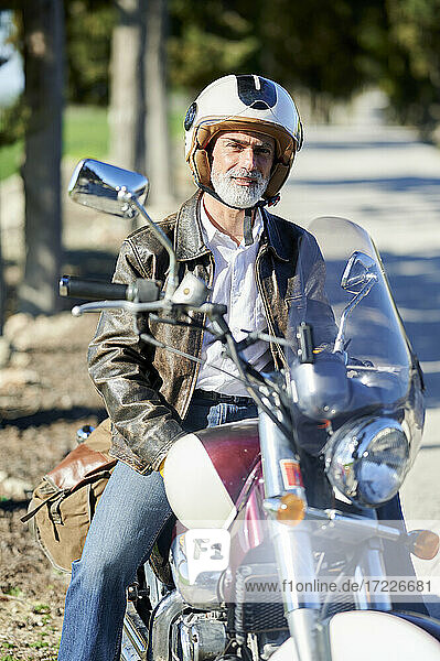 Älterer Mann mit Sturzhelm auf einem Motorrad sitzend während einer Autofahrt