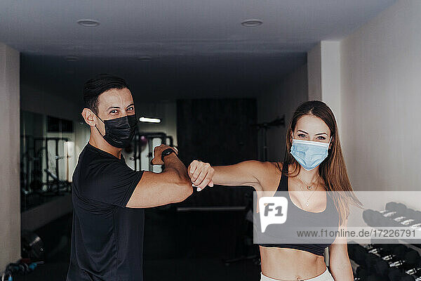Sportler mit Schutzmaske grüßt mit einem Freund im Fitnessstudio durch Ellbogenstöße