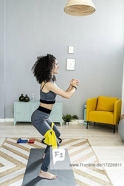 Smiling woman looking away while exercising with resistance band in living room