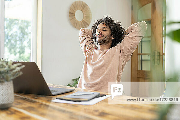 Male entrepreneur relaxing with hands behind head while laptop on table at home