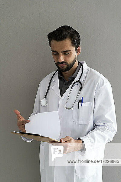 Male doctor reading medical report in front of wall