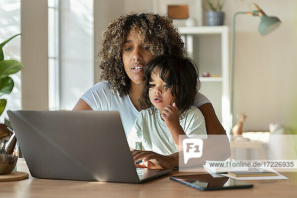 Mutter und kleine Tochter schauen gemeinsam auf den Laptop  während sie von zu Hause aus arbeiten