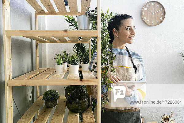 Schöne Gärtnerin mit digitalem Tablet  die wegschaut  während sie neben einem Regal in einer Werkstatt steht