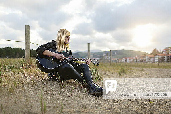 Musikerin spielt Gitarre  während sie auf Sand sitzt