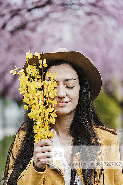 Lächelnde Frau mit geschlossenen Augen,  die im Frühling gelbe Blumen hält