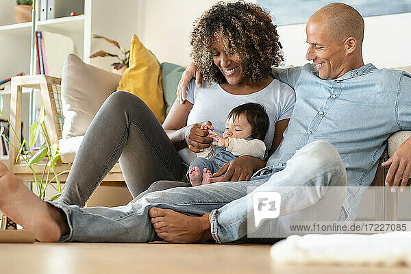 Lächelnde Mutter und Vater betrachten das Baby  während sie zu Hause auf dem Boden sitzen
