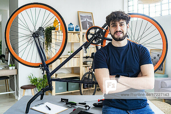 Lächelnder junger Mann  der zu Hause mit dem Fahrrad auf dem Tisch sitzt