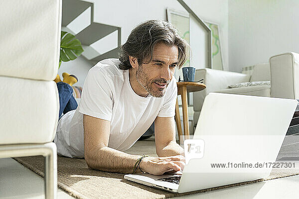 Mann benutzt Laptop  während er zu Hause auf dem Boden liegt