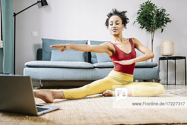 Frau macht Yoga  während sie zu Hause auf dem Laptop ein Online-Tutorial ansieht