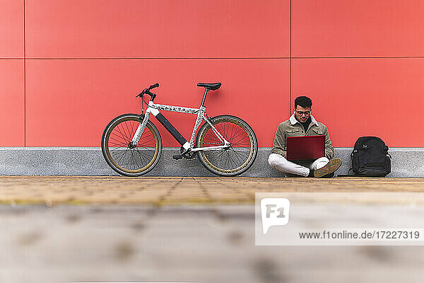 Geschäftsmann  der einen Laptop benutzt  während er mit dem Fahrrad auf dem Gehweg sitzt