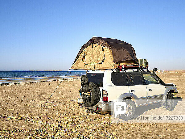 Tent pitched on top of roof of off-road vehicle parked on sandy coastal beach