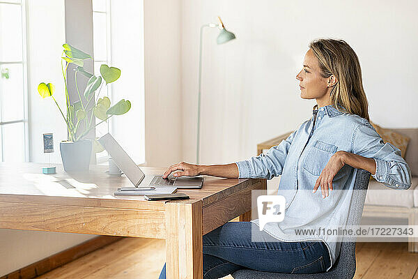 Nachdenkliche Geschäftsfrau  die wegschaut  während sie am Schreibtisch im Heimbüro sitzt