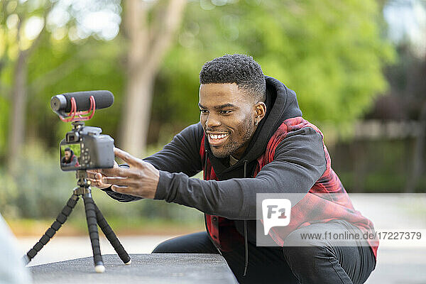 Lächelnder männlicher Vlogger  der die Kamera auf einem Stativ in einem öffentlichen Park einstellt