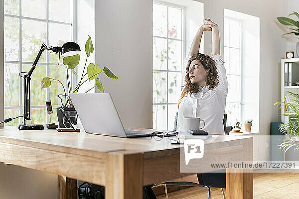 Weibliche Unternehmerin streckt die Hände am Schreibtisch im Heimbüro aus
