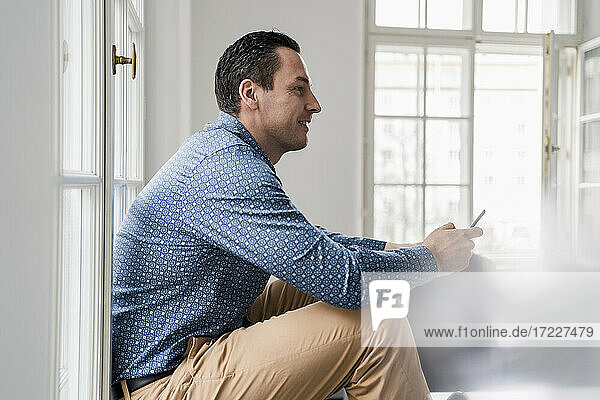 Männlicher Unternehmer  der im Büro sitzend ein Smartphone benutzt