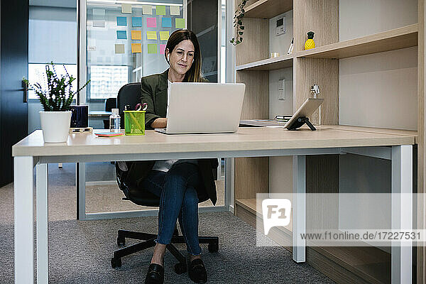 Concentrated female entrepreneur working on laptop while sitting at desk in office