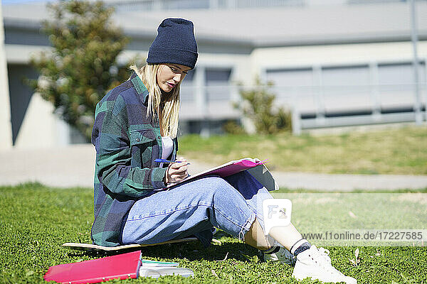 Junge Frau studiert auf dem Skateboard sitzend auf einem College-Campus an einem sonnigen Tag