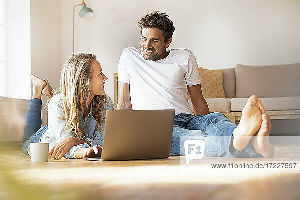 Mid adult couple with laptop looking at each other at home