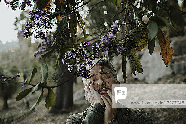 Älterer Mann  der sein Gesicht berührt  während er unter einem blühenden Baum im Garten steht