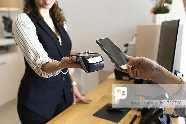 Geschäftsfrau hält Mobiltelefon an Kreditkartenleser an der Hotelrezeption