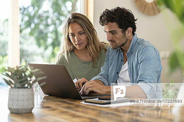 Man using laptop while sitting by girlfriend at table