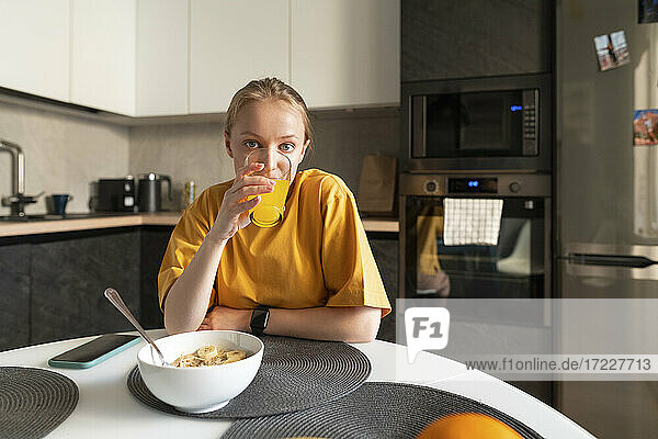 Woman drinking juice while sitting by table at home