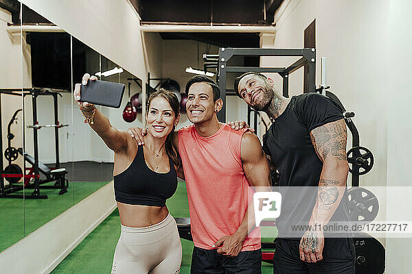 Lächelnde Sportlerin  die ein Selfie mit ihren männlichen Freunden im Fitnessstudio macht