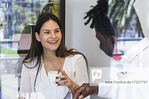 Junge Geschäftsfrau lächelt ihren Mitarbeiter an  während sie in einem Café Kaffee trinkt