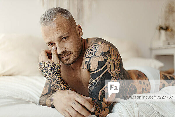 Ernster Mann mit Tattoo auf dem Bett liegend zu Hause