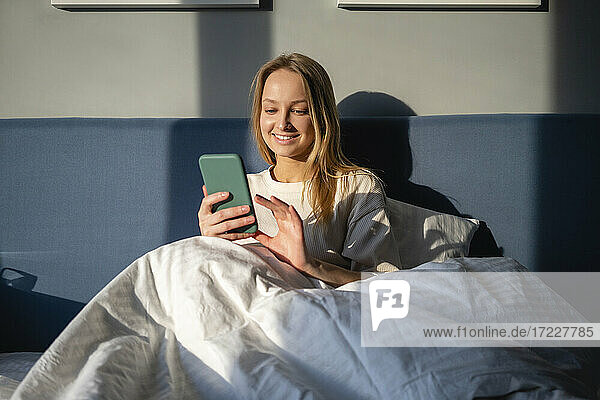 Sunlight on smiling woman using smart phone while sitting at home