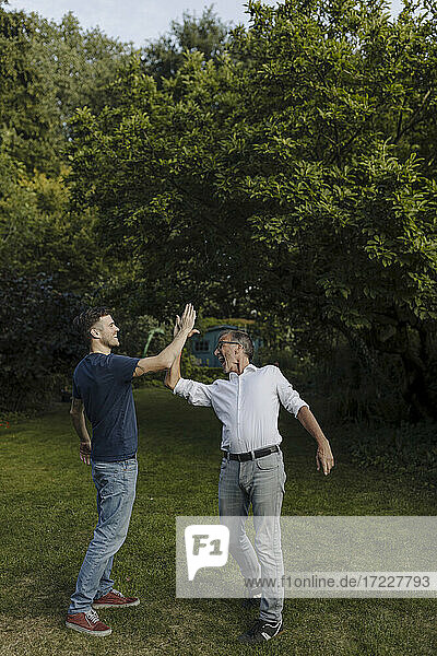 Lachender Vater und Sohn beim High-Five im Hinterhof stehend