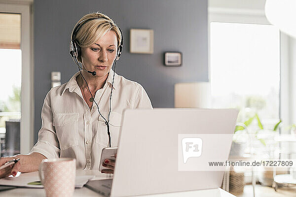 Mature businesswoman in headset on video call through laptop in home office