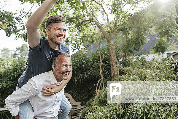 Father giving piggyback ride to cheerful son in backyard