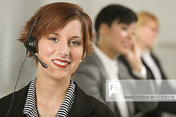 Pretty red haired businesswoman with headset and colleagues behind in office setting
