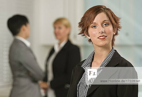 Hübsche rothaarige Geschäftsfrau mit Kollegen hinten in einer Büroumgebung